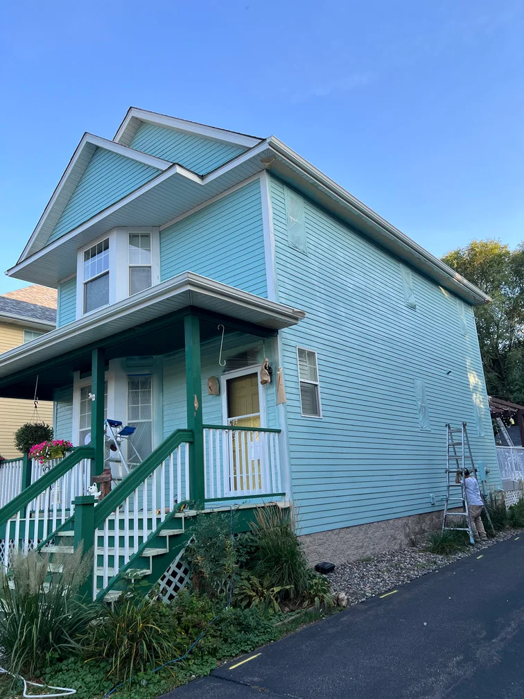Light blue house with white trim, green porch posts, and white railings on two-story home
