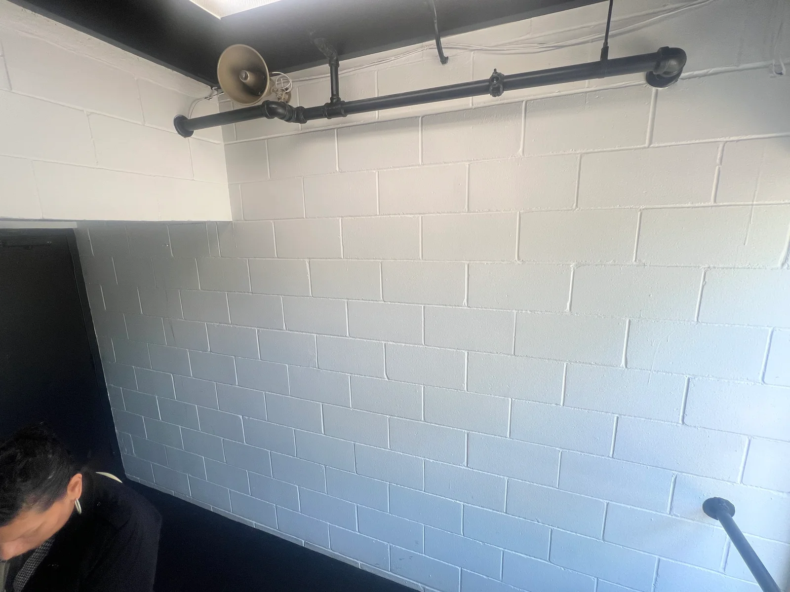 White painted concrete block basement wall with black pipe and industrial lighting fixture