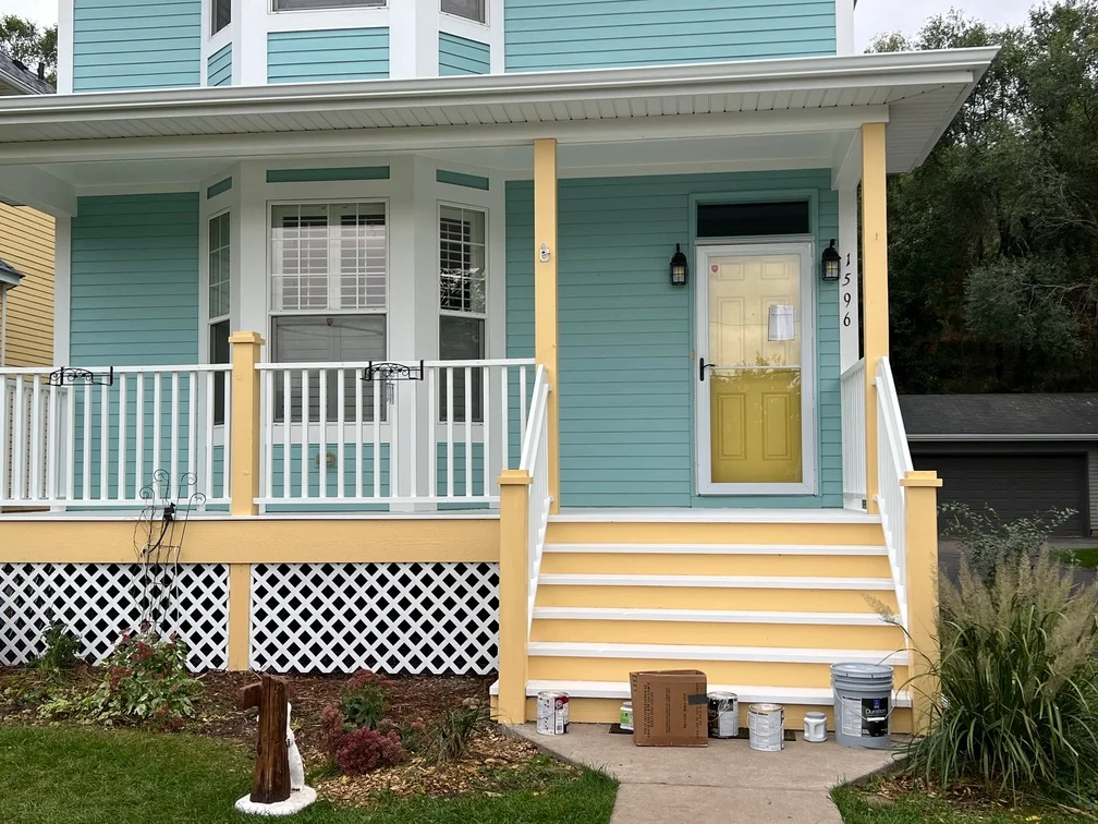 Turquoise house exterior with white trim, yellow columns, and yellow entry door on front porch