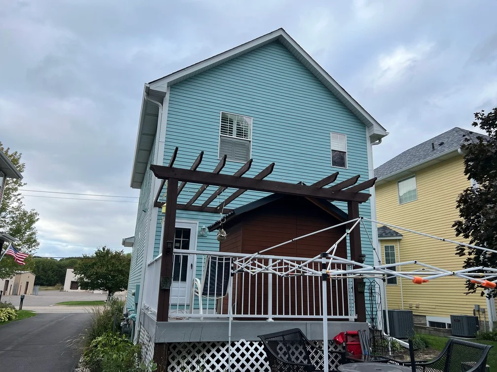 Light blue painted house exterior with dark wood pergola and white deck railings