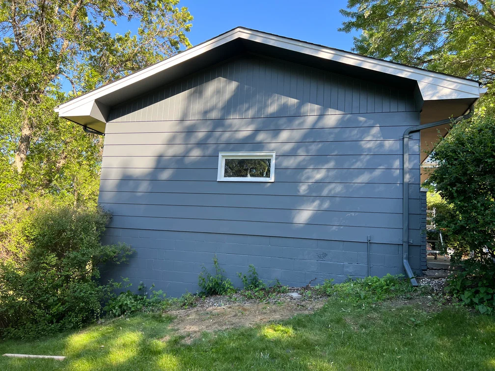Freshly painted garage with light blue-gray horizontal siding and dark charcoal gable end