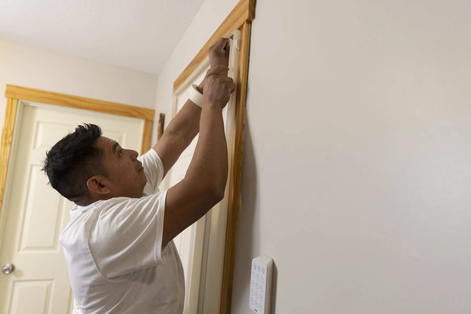 Painter applying finish to wooden door frame trim with white walls