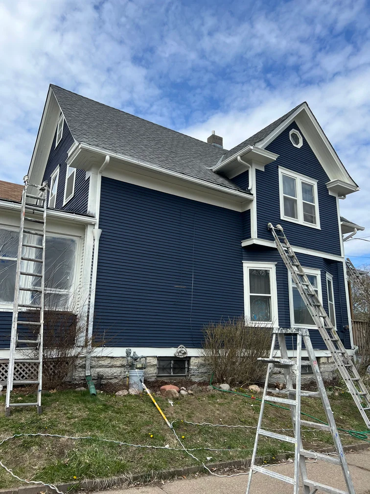 Two-story house with freshly painted navy blue siding and white trim, work ladders in place