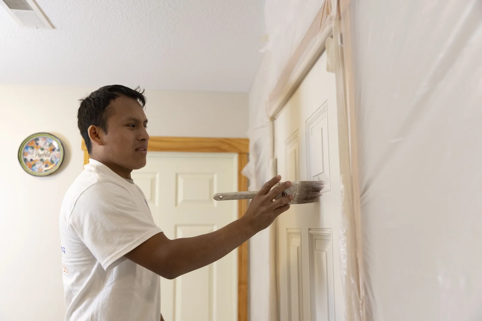 Painter applying white paint to interior wall with brush near door frame