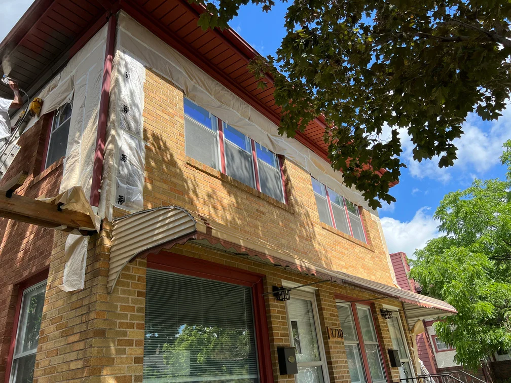 Brick house exterior with protective plastic sheeting on windows during painting project