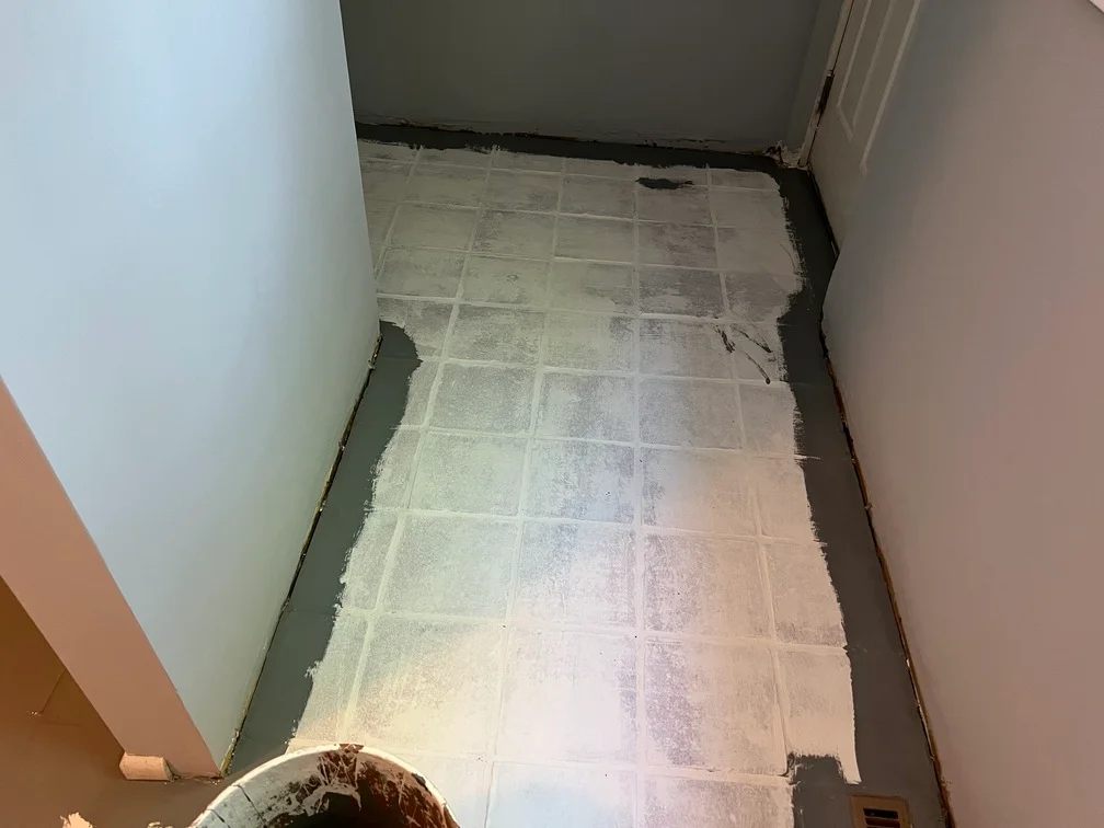 Ceramic tile floor with gray primer coating and white painter's tape along edges