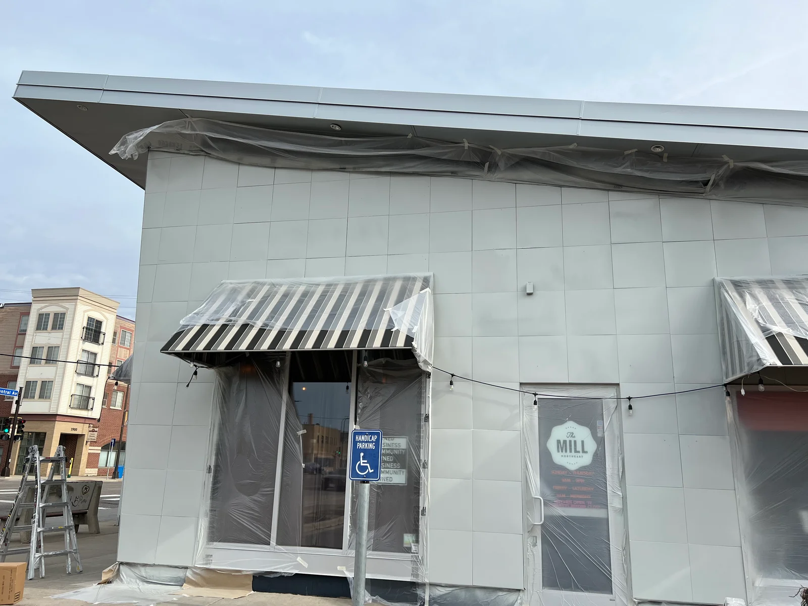 Commercial storefront with gray fiber cement panel exterior and striped awning during painting project