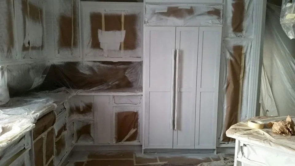 White painted kitchen cabinets with drywall prep, masked surfaces, and protective coverings