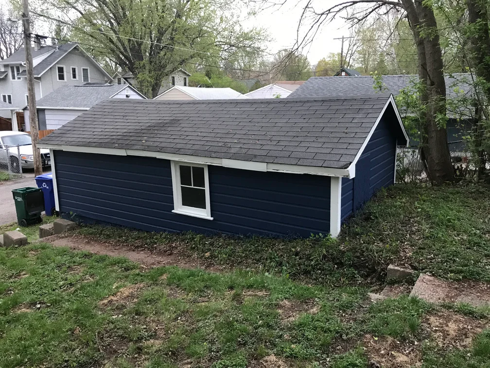 Dark blue painted garage with white trim, new asphalt shingle roof, horizontal siding