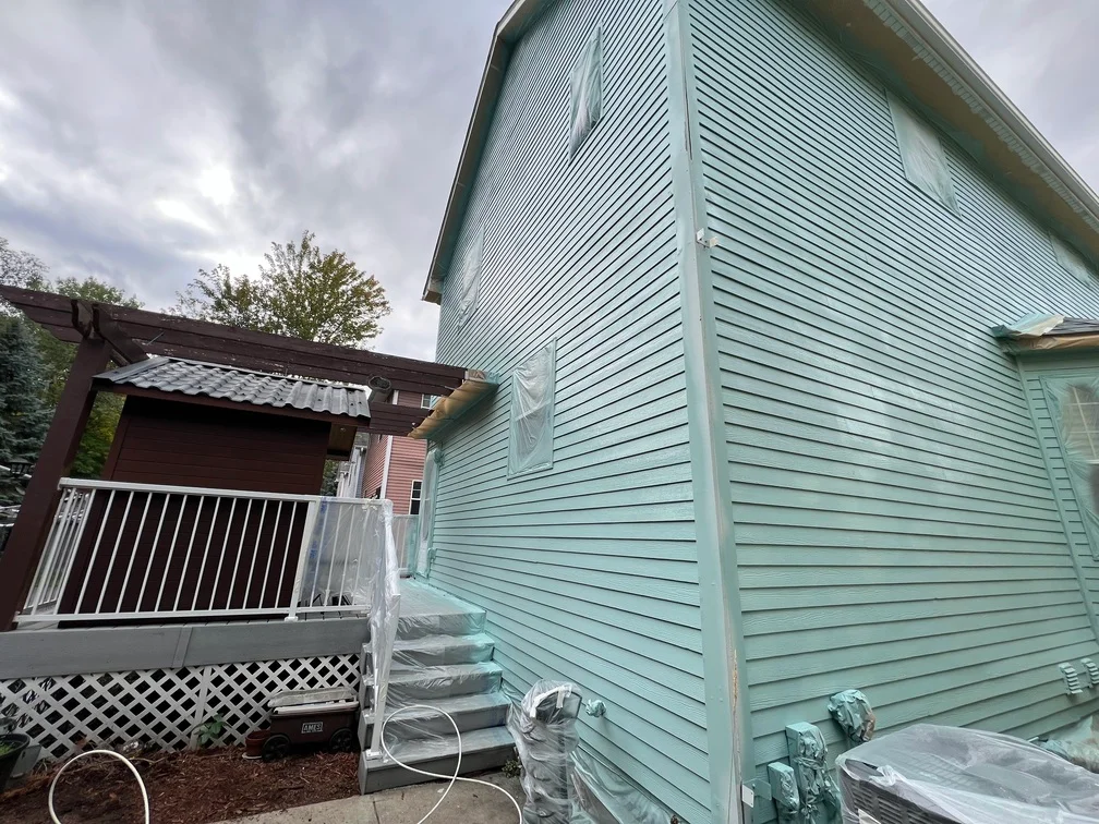Freshly painted mint-green vinyl siding on residential home exterior with white trim and deck