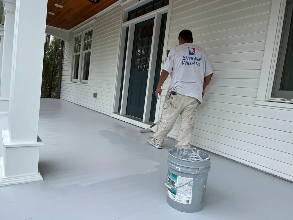 Painter applying white paint to vinyl siding and trim on residential home exterior