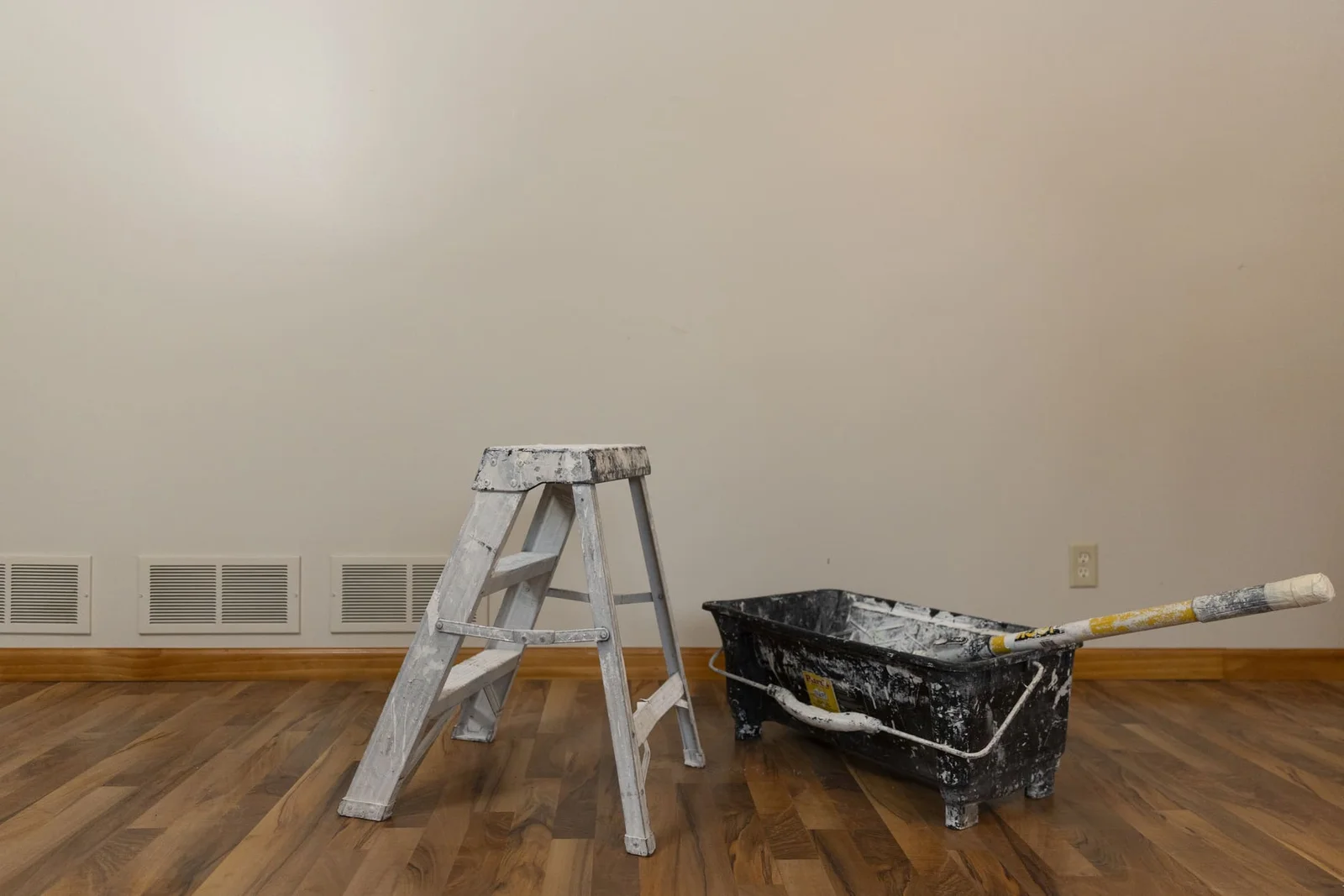 Interior room with primed walls, wooden floors, ladder, and paint bucket ready for painting work