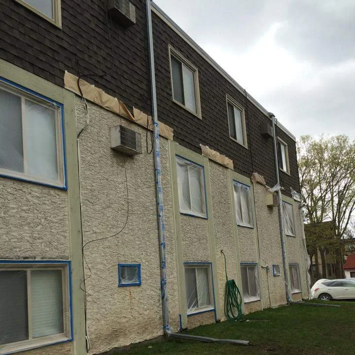 Multi-story residential building with cream stucco and dark shingle siding, freshly painted exterior