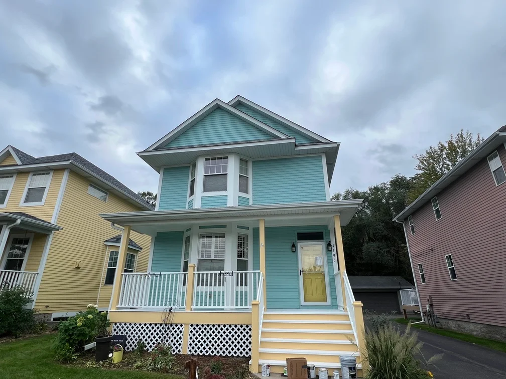 Turquoise two-story house with white trim, yellow porch columns, and yellow door after exterior painting
