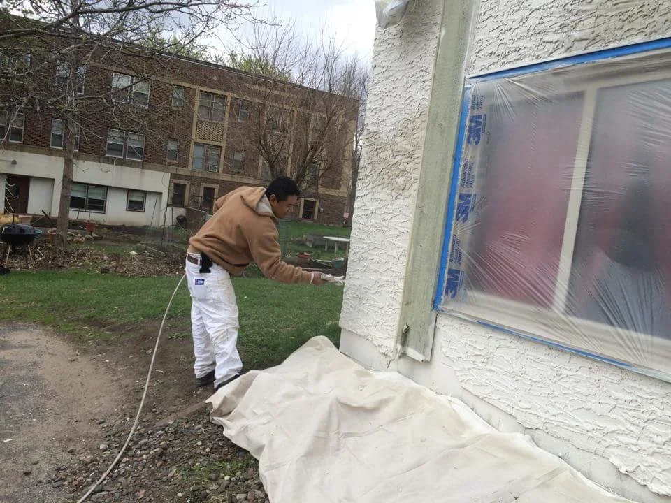 Painter masking stucco exterior wall with blue tape and drop cloth protection