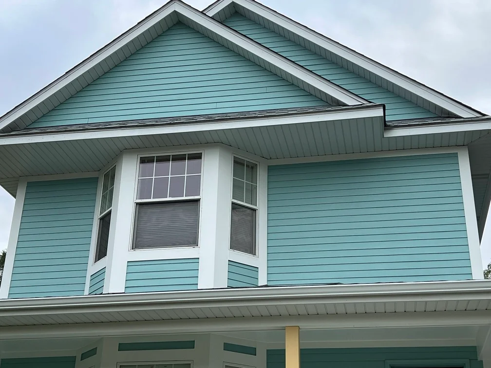 Turquoise painted house siding with white trim, gable roof, and multi-pane windows