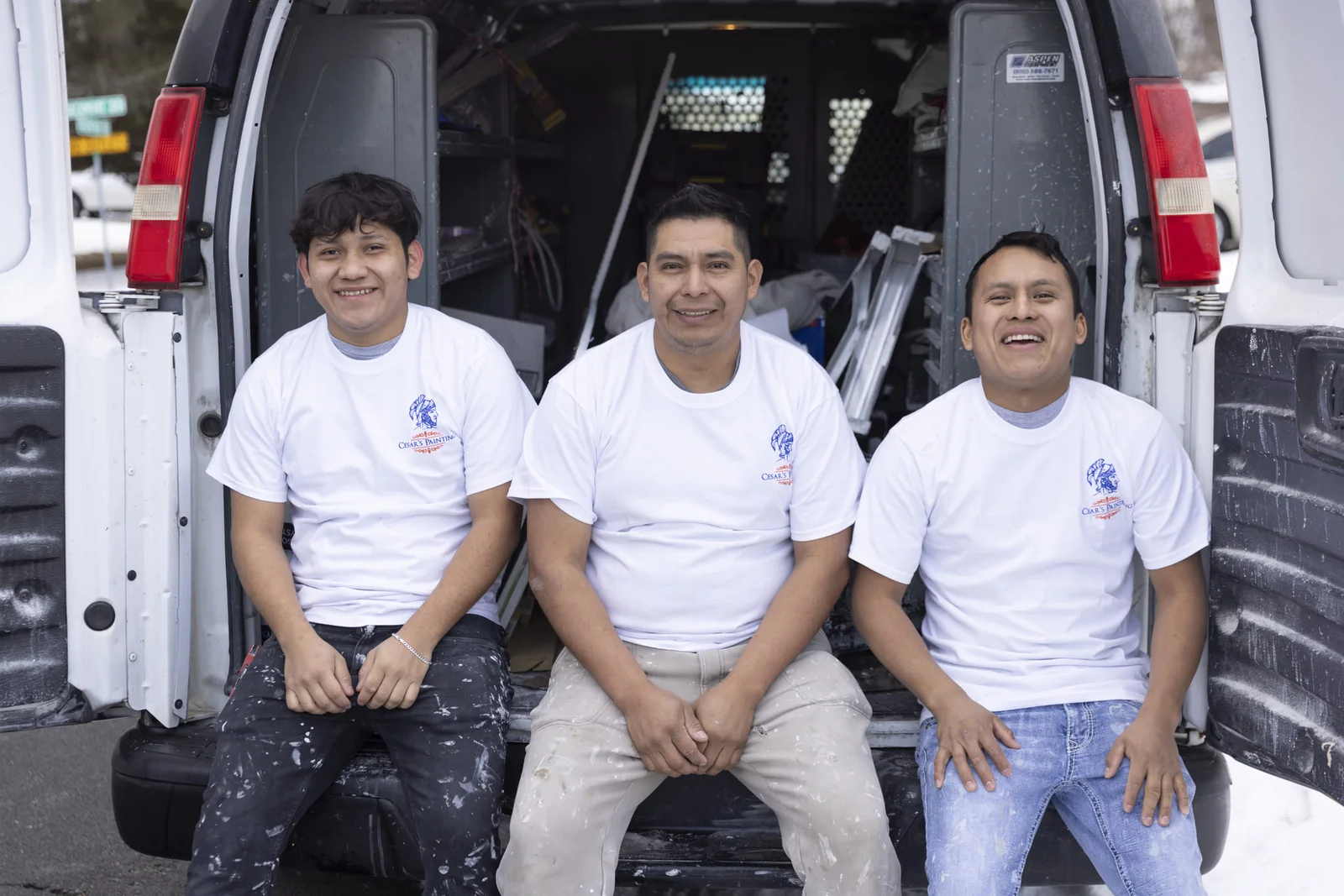 Three painters in branded white shirts seated at service van with equipment and tools visible