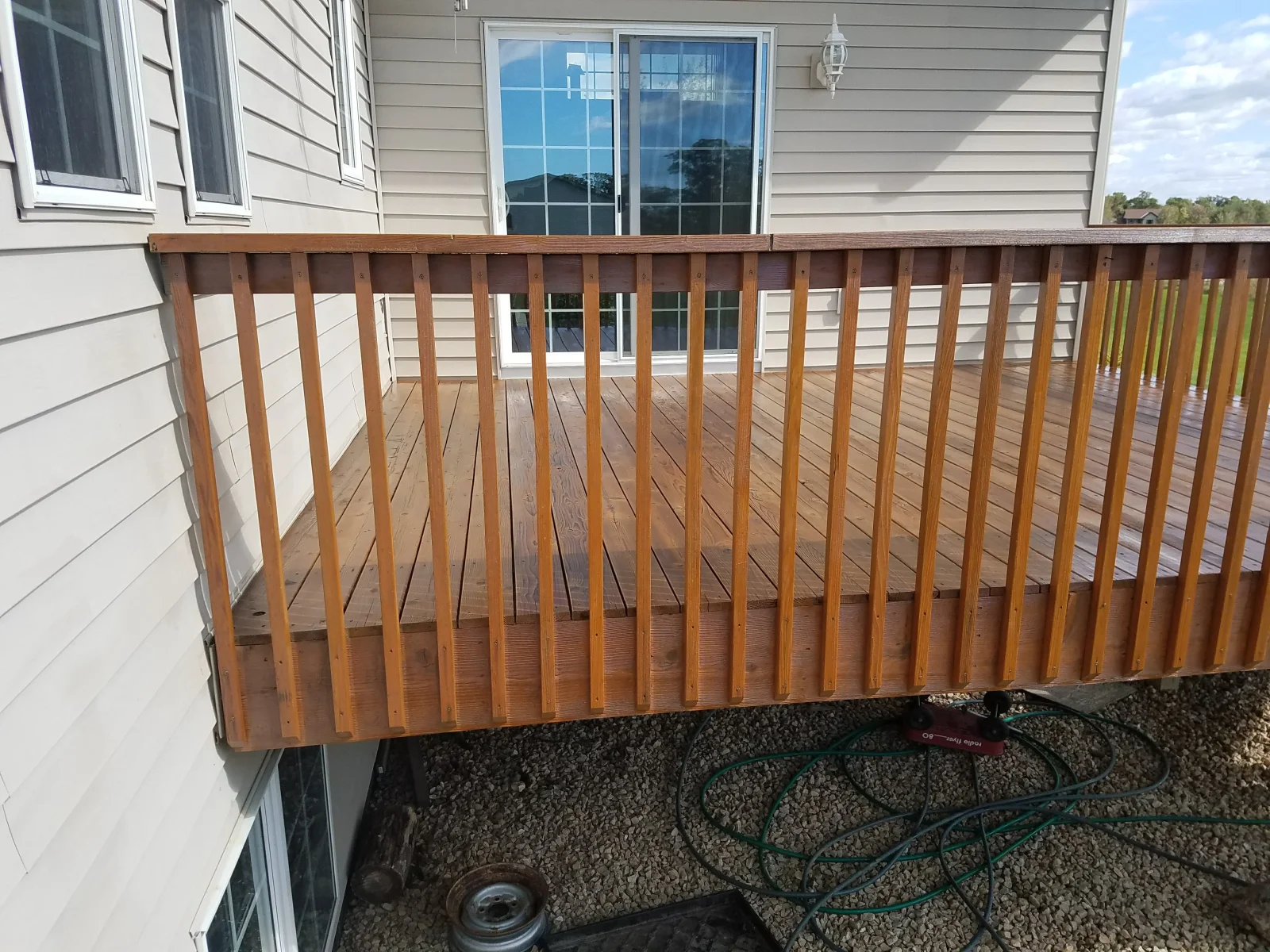 Stained wood deck with vertical baluster railing and sliding glass doors
