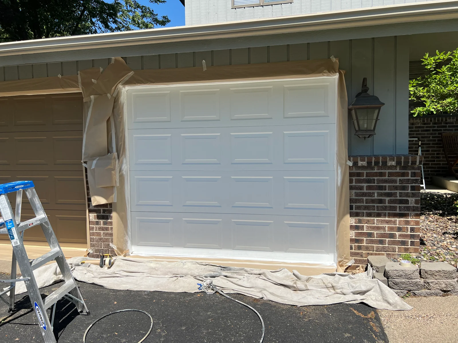 White painted garage door with multi-panel design, protective coverings and ladder visible during painting project