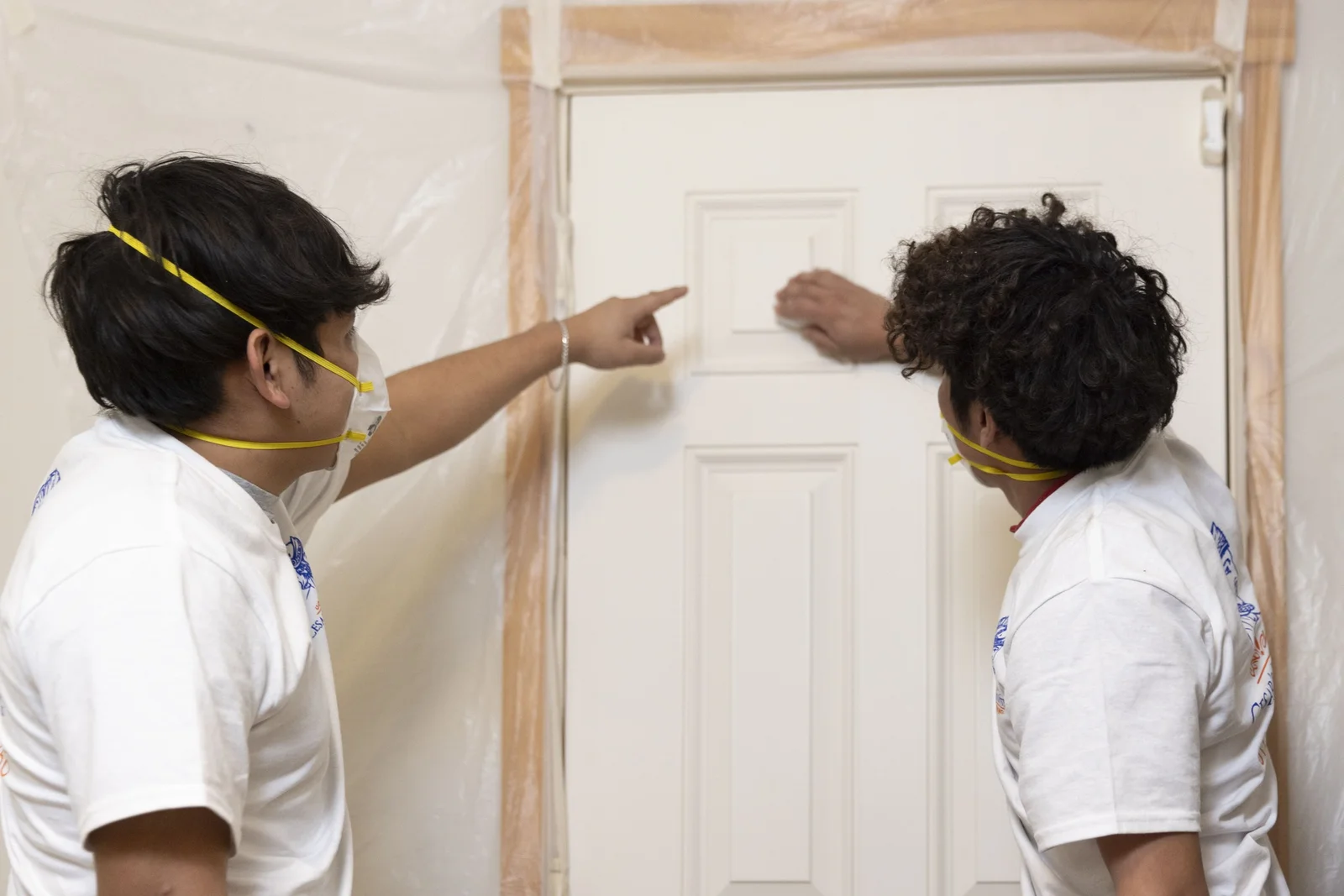 Two workers measuring and installing six-panel interior door with wood frame trim