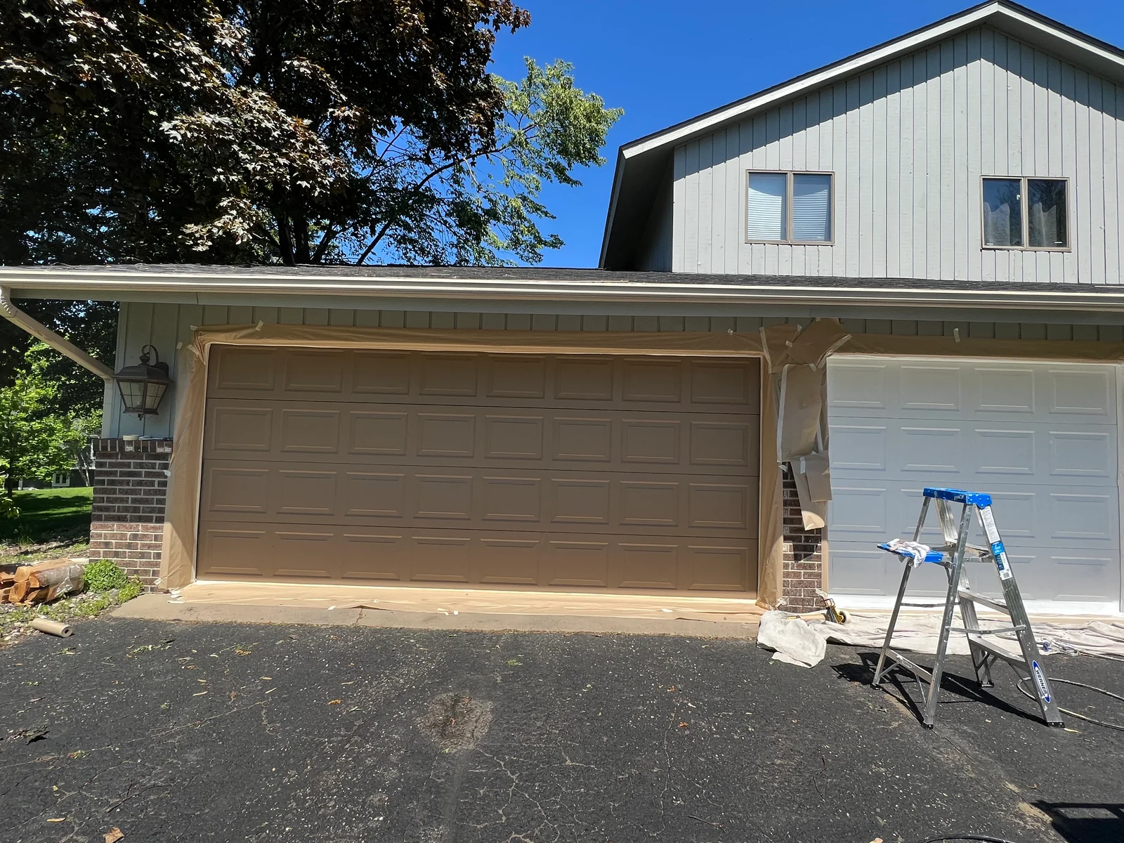Tan-painted garage door frame with protective masking on white garage doors and brick home exterior