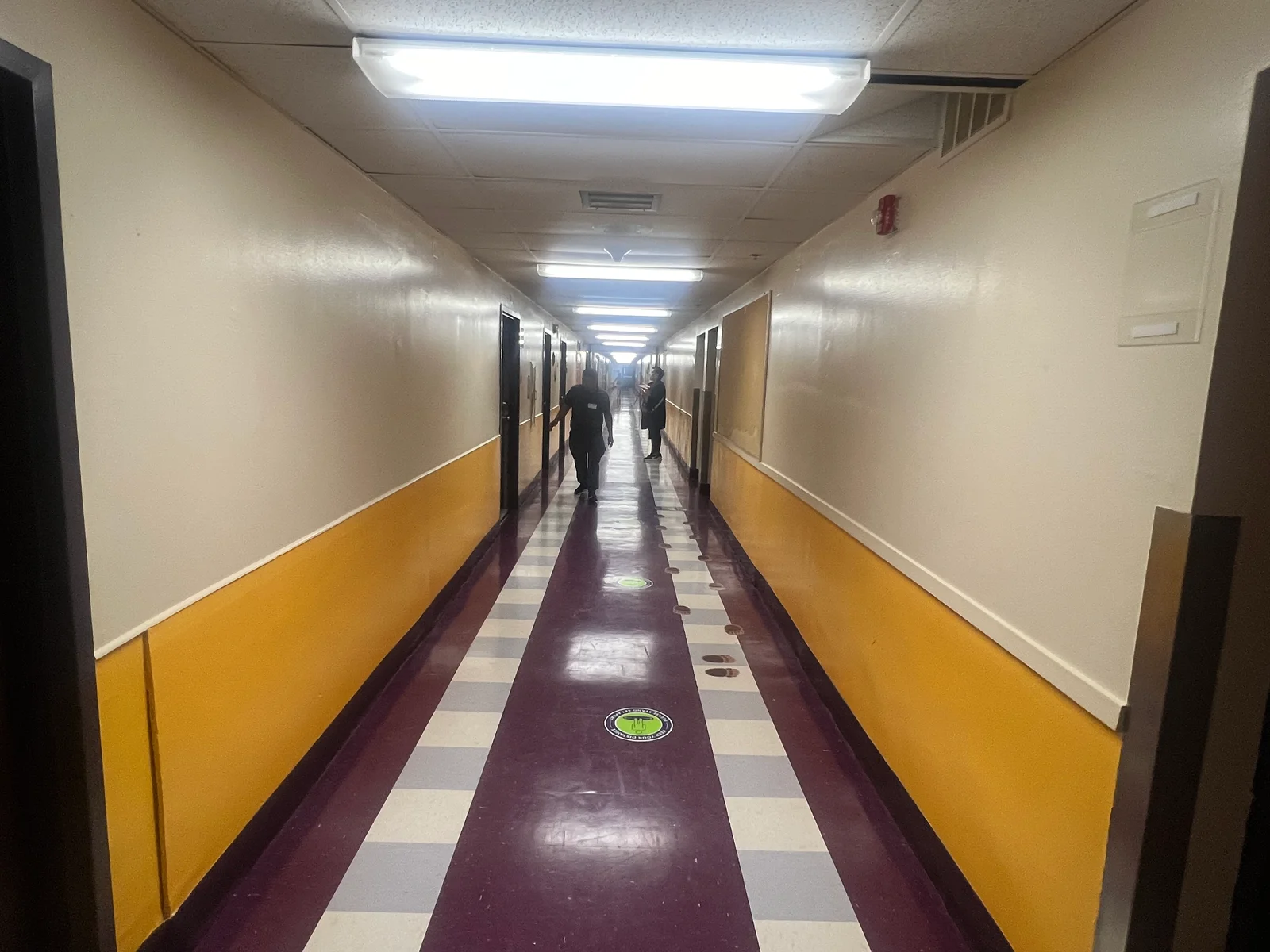 Long hallway with cream and yellow two-tone painted walls, burgundy and beige checkered floor, LED ceiling lights