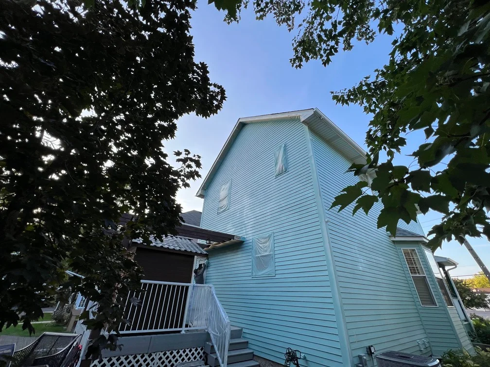 Light blue painted vinyl siding on two-story residential home with white trim and deck