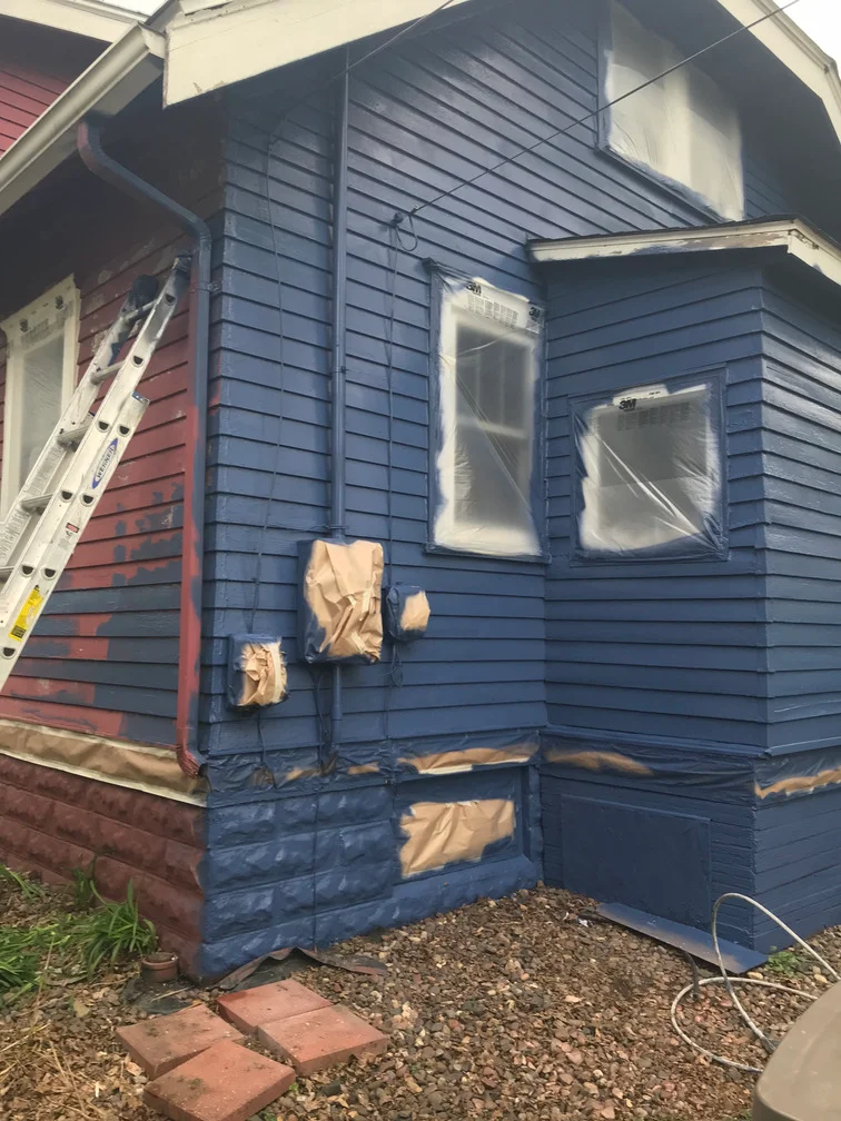 Navy blue exterior house paint applied to horizontal lap siding with masked windows and protective coverings