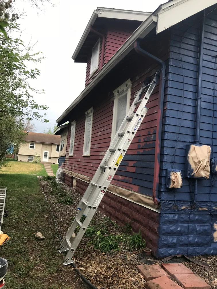 Exterior house painting with burgundy and navy siding, ladder setup, protective coverings