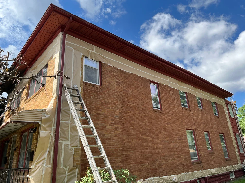 Brick building exterior with protective plastic sheeting and aluminum ladder for painting prep