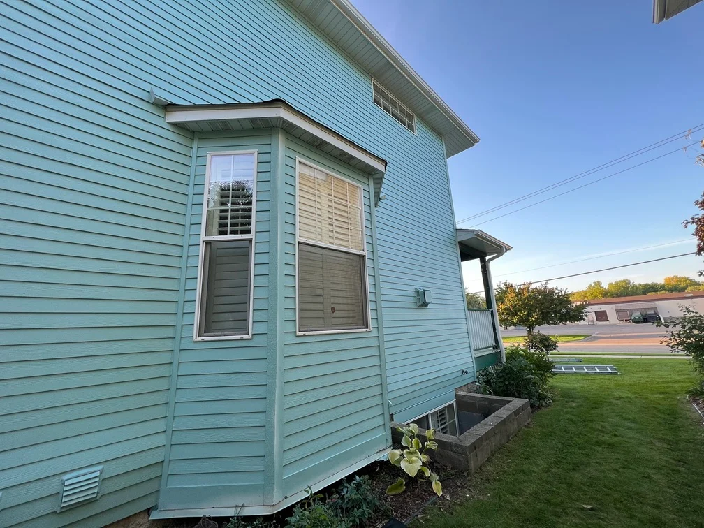 Light blue-green painted vinyl siding with white trim and window frames on residential home exterior