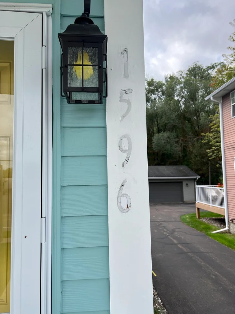 Turquoise horizontal siding with white trim, black lantern, and house numbers on exterior wall