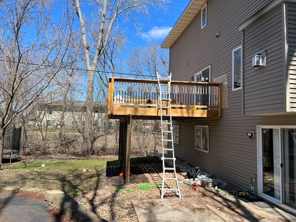 Elevated wooden deck with metal spindle railing and access ladder attached to house