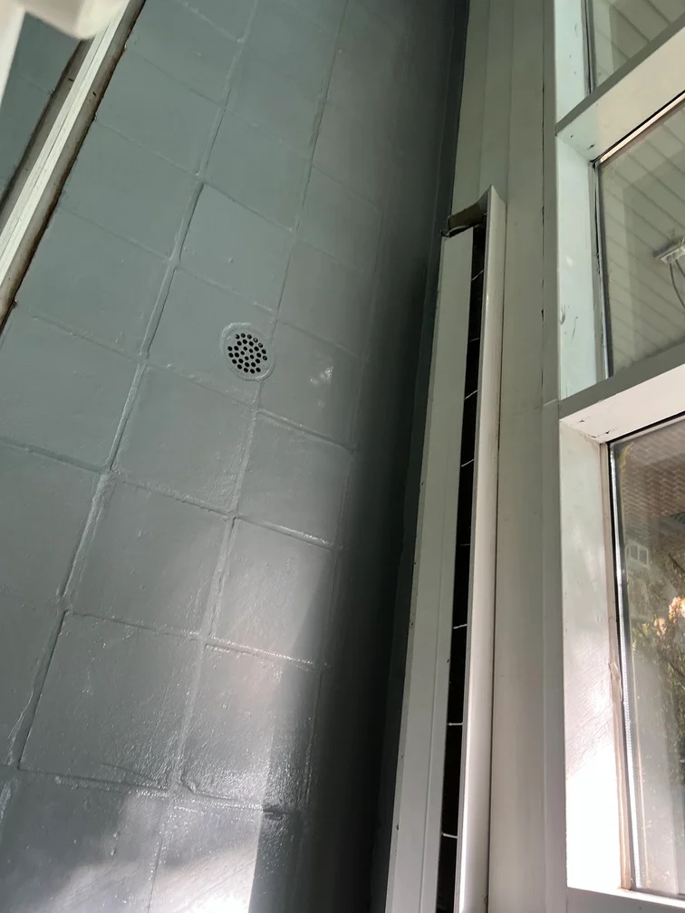 Gray painted bathroom wall with tile pattern, ventilation vent, and white trim molding