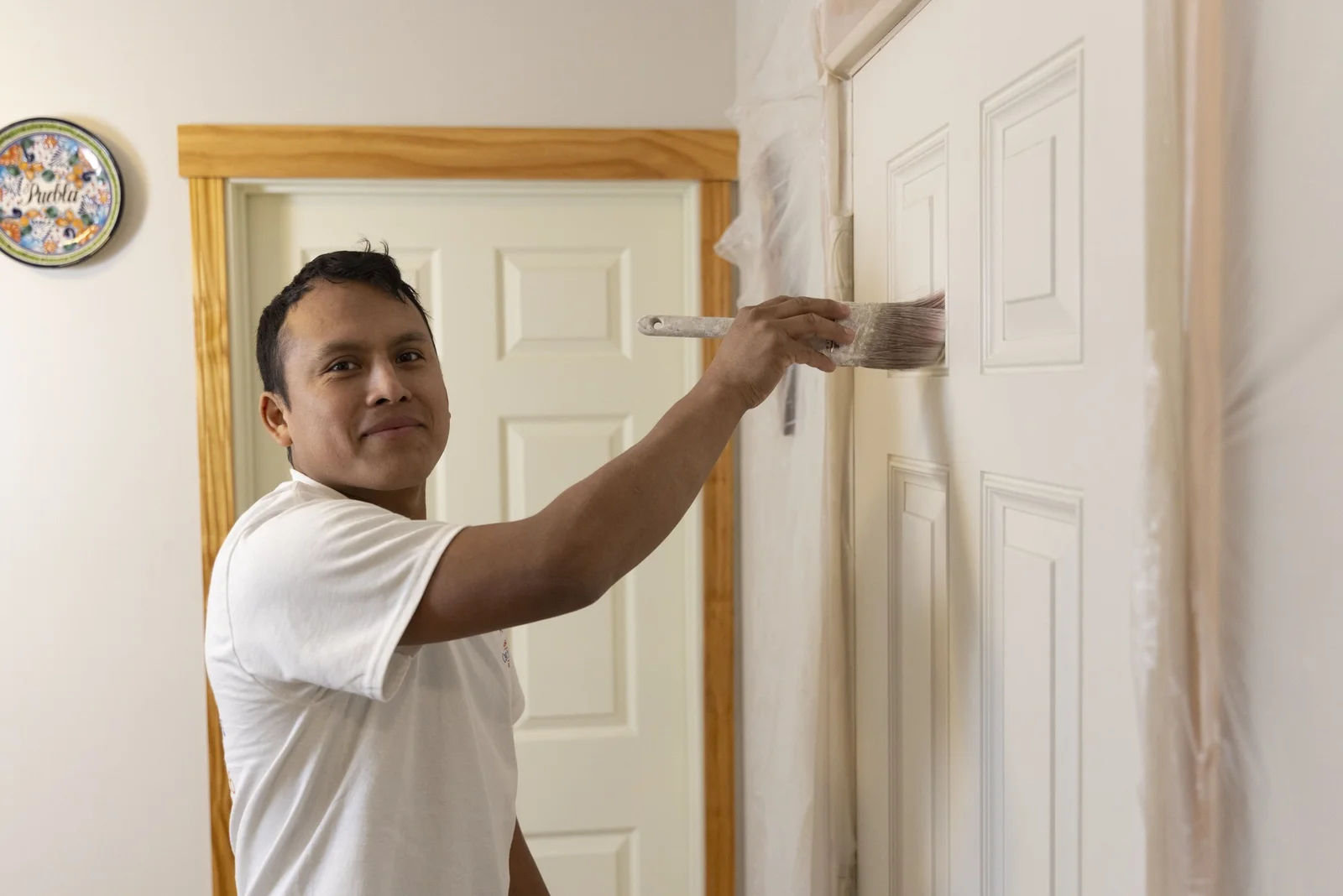 Painter applying finish coat to white six-panel interior door trim with brush