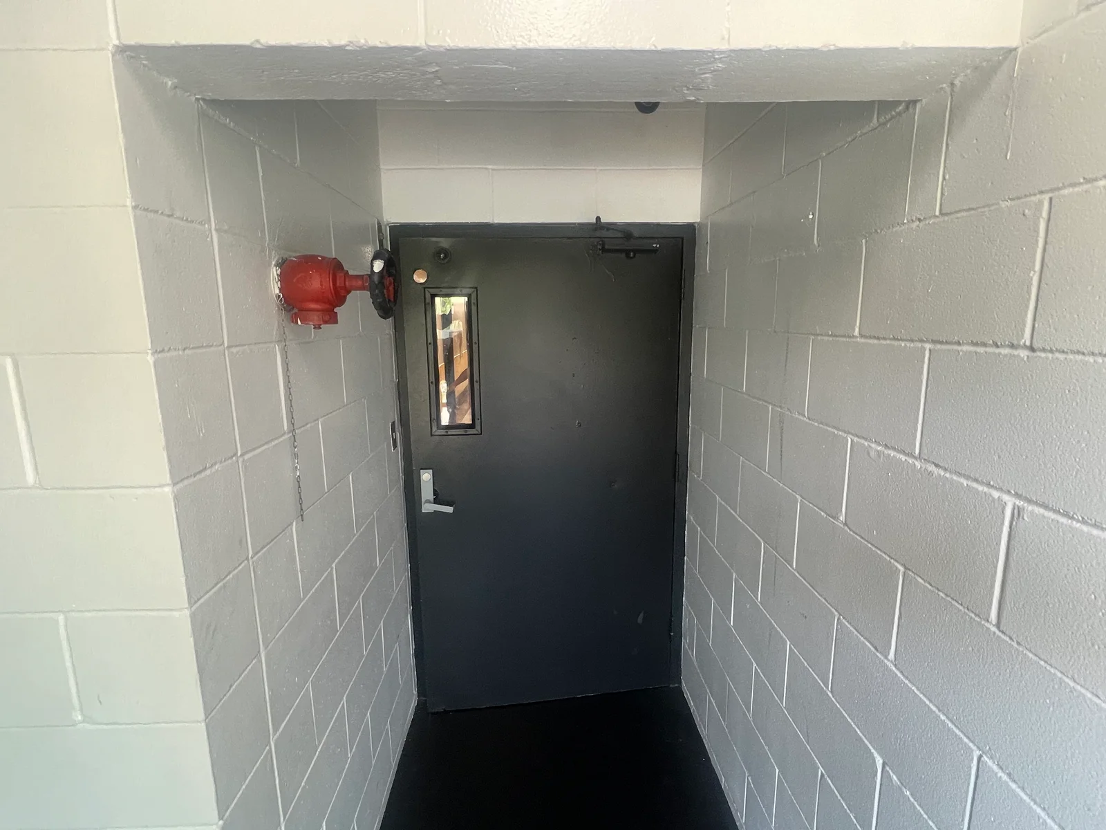 Painted concrete block stairwell with gray walls, white trim, black door, and red fire alarm