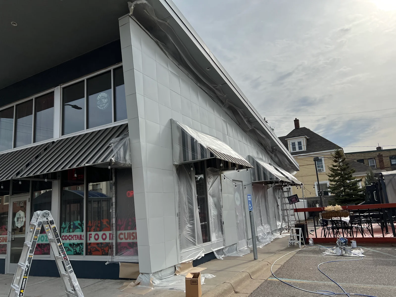 Commercial building exterior with white fiber cement panels, protective plastic sheeting, and professional painting preparation setup